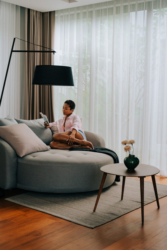 Woman reading on a sofa inside a bright luxury suite, highlighting comfort and lifestyle storytelling in hospitality.